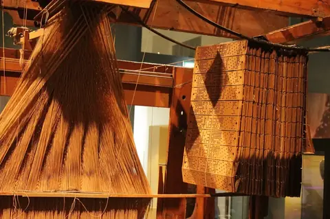 雅卡尔织布机与挂在机上的打孔卡（苏格兰国家博物馆藏）。换一叠卡片，同一台机器就织出另一种花。